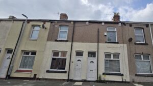 Property for sale by Auction A row of terraced houses with different colored facades under a cloudy sky. Each house has a distinct door and window design, some with satellite dishes and chimneys. The ground is paved with concrete. Presented by Palace Auctions