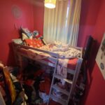 Property for sale by Auction A small, cluttered bedroom with bright pink walls features a bunk bed covered in toys and clothes. Piles of clothes are on the floor. A poster of animated characters hangs on the wall, and a window with light curtains is partially open. Presented by Palace Auctions