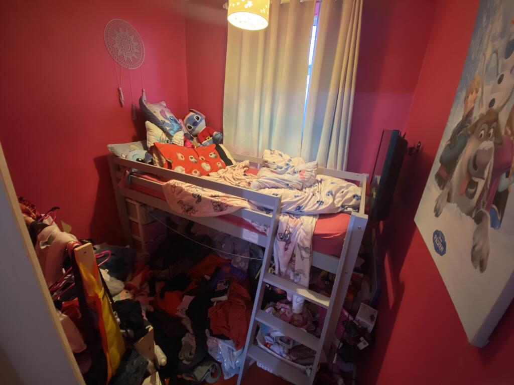 Property for sale by Auction A small, cluttered bedroom with bright pink walls features a bunk bed covered in toys and clothes. Piles of clothes are on the floor. A poster of animated characters hangs on the wall, and a window with light curtains is partially open. Presented by Palace Auctions