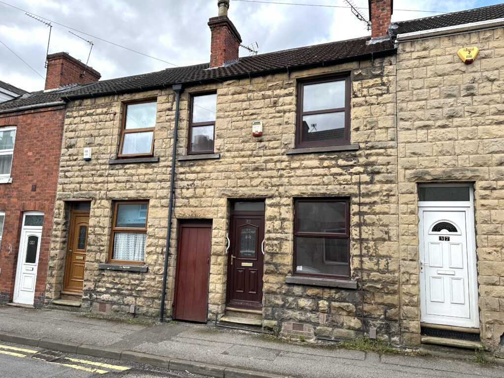 Property for sale by Auction A row of traditional terraced houses with stone facades and chimneys, featuring three front doors in different colors: brown, maroon, and white. The street is quiet, with a cloudy sky overhead. Presented by Palace Auctions