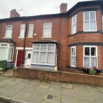 Property for sale by Auction A row of red brick terraced houses with bay windows and a small front garden. The pavement in front is concrete, and a red car is partially visible on the left. There are white net curtains in the windows. Presented by Palace Auctions