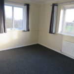 Property for sale by Auction A small empty room with light-colored walls and two windows. The floor is carpeted in dark gray, and there's a white radiator under one window. The windows have dark curtains and offer a view of trees and grass outside. Presented by Palace Auctions