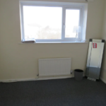 Property for sale by Auction Empty room with beige walls and a gray carpet. A window with a blind is on one wall, with a lamp and some papers on the windowsill. A tall mirror and a wastebasket are positioned against another wall under the window. Presented by Palace Auctions