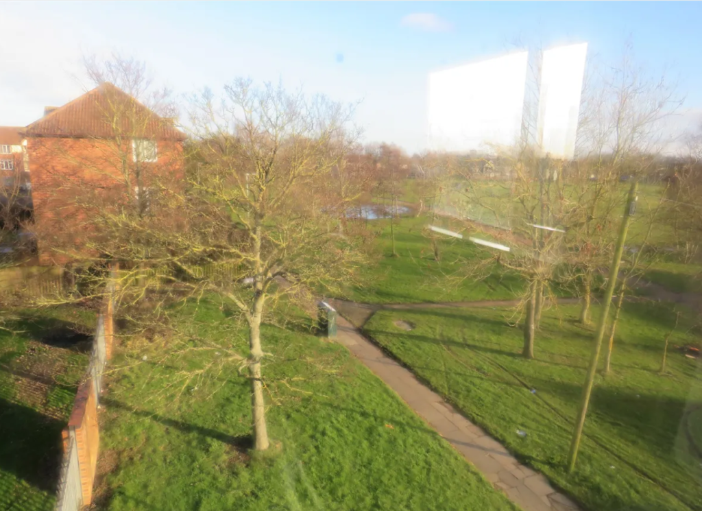 Property for sale by Auction View of a park with leafless trees and green grass, intersected by paved walkways. A red brick building is partially visible on the left. The sky is clear and the scene is sunlit, creating a bright, reflective atmosphere. Presented by Palace Auctions