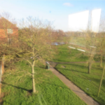 Property for sale by Auction View of a park with leafless trees and green grass, intersected by paved walkways. A red brick building is partially visible on the left. The sky is clear and the scene is sunlit, creating a bright, reflective atmosphere. Presented by Palace Auctions