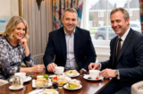 Property for sale by Auction Three people are seated at a table enjoying afternoon tea. The table has teacups, sandwiches, and desserts. They are smiling in business attire, sitting in a cozy room with floral curtains—a serene pause from discussing how Palace Auctions London expands its probate property auction services. Presented by Palace Auctions