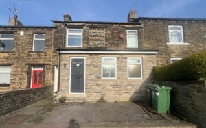Property for sale by Auction A row of two-story brick townhouses with chimneys. The house in the center has a blue front door and white-framed windows. To the right, there's a green waste bin near a stone wall. The sky is clear and sunny. Presented by Palace Auctions