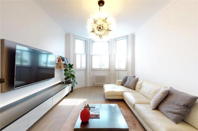 Property for sale by Auction Experience luxury living in a modern Earls Court apartment for sale, featuring a chic living room with a beige sectional sofa, gray cushions, and a wooden coffee table. Enjoy the ambiance created by large windows and a decorative chandelier illuminating the space. Presented by Palace Auctions