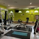 Property for sale by Auction A gym with green walls featuring various exercise equipment, including weight benches, a weight rack, stationary bike, and dumbbells. Mats are placed on the floor, and mirrors line one wall. Presented by Palace Auctions