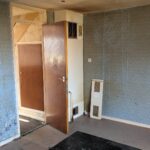 Property for sale by Auction An empty, run-down room with peeling blue wallpaper, a partially open wooden door, and a small space heater on the floor. The floor is bare and worn, and there are signs of water damage on the wall. Presented by Palace Auctions