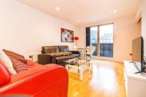 Property for sale by Auction Modern living room with red and black sofas, a glass coffee table, a flat-screen TV on a white stand, and a dining area with glass-top table and chairs. Large window offers cityscape view. Bright artwork decorates the wall. Presented by Palace Auctions