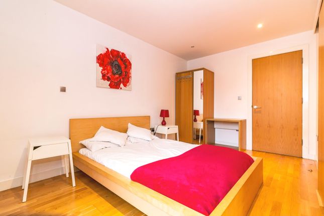 Property for sale by Auction A minimalist bedroom with a wooden bed, white bedding, and a red blanket. Two small white nightstands with red lamps flank the bed. A wardrobe and a desk are against the wall. A painting of a red flower hangs above the bed on a white wall. Presented by Palace Auctions