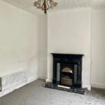 Property for sale A mostly empty room with white walls, grey carpet, a black ornate fireplace, radiator on the left wall, and a decorative ceiling light fixture in this Stanley property for sale. Presented by Palace Auctions