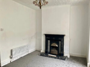 Property for sale A mostly empty room with white walls, grey carpet, a black ornate fireplace, radiator on the left wall, and a decorative ceiling light fixture in this Stanley property for sale. Presented by Palace Auctions