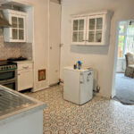 Property for sale A kitchen with patterned tile flooring, white cabinets, a small white fridge, stove, and a stainless steel sink. An adjacent room with carpet and a single patterned chair is visible—ideal for a Rose Avenue family home in County Durham. Presented by Palace Auctions
