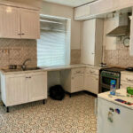 Property for sale A kitchen in a Stanley 3-bed terrace with white cabinets, a tile backsplash, gas stove and oven, stainless steel range hood, small fridge, patterned floor tiles, window blinds, and various items on the counters. Presented by Palace Auctions