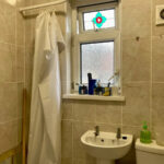 Property for sale A small tiled bathroom in a Stanley 3-bed terrace, featuring a shower curtain, frosted window with colorful design, twin-tap sink, toiletries on the sill, soap dispenser, and wall-mounted extractor fan—perfect for a County Durham house auction. Presented by Palace Auctions