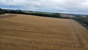 Property for sale A wide, harvested field under a cloudy sky stretches towards a line of distant trees and rolling hills—an ideal setting for speculative development land in Lane End, High Wycombe, with patches of greenery on the horizon. Presented by Palace Auctions
