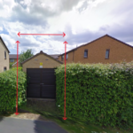 Property for sale A brown garage with black doors sits between green hedges, marked by red arrows showing its height and width—an ideal alternative real estate asset. Houses and a street appear in the background under a cloudy sky. Presented by Palace Auctions