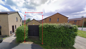Property for sale A brown garage with black doors sits between green hedges, marked by red arrows showing its height and width—an ideal alternative real estate asset. Houses and a street appear in the background under a cloudy sky. Presented by Palace Auctions