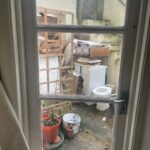 Property for sale View through a window reveals a cluttered outdoor area at Gwydyr Mansions Brighton, with a washing machine, boxes, wooden items, potted plant, and debris on concrete. Stairs and railings are seen—potential investment property Brighton opportunity. Presented by Palace Auctions