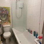 Property for sale A small bathroom in Gwydyr Mansions Brighton features a bathtub, wall-mounted shower, toilet, and toiletries on the tub edge. Above the toilet hangs a colorful painting of a person in a headdress. A towel and mat are also visible. Presented by Palace Auctions