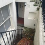 Property for sale A narrow brick staircase with black railings leads down to a basement entrance of a white building—an ideal investment property Brighton seekers will appreciate. The ground is damp with scattered leaves, and a door is visible at the bottom. Presented by Palace Auctions