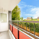 Property for sale A bright balcony with red railing panels overlooks green trees and homes, perfect for a buy-to-let in West Bridgford. A white door and windows lead inside this inviting one-bedroom flat, set under a blue sky with scattered clouds. Presented by Palace Auctions