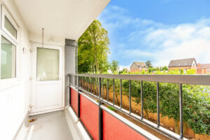 Property for sale A bright balcony with red railing panels overlooks green trees and homes, perfect for a buy-to-let in West Bridgford. A white door and windows lead inside this inviting one-bedroom flat, set under a blue sky with scattered clouds. Presented by Palace Auctions