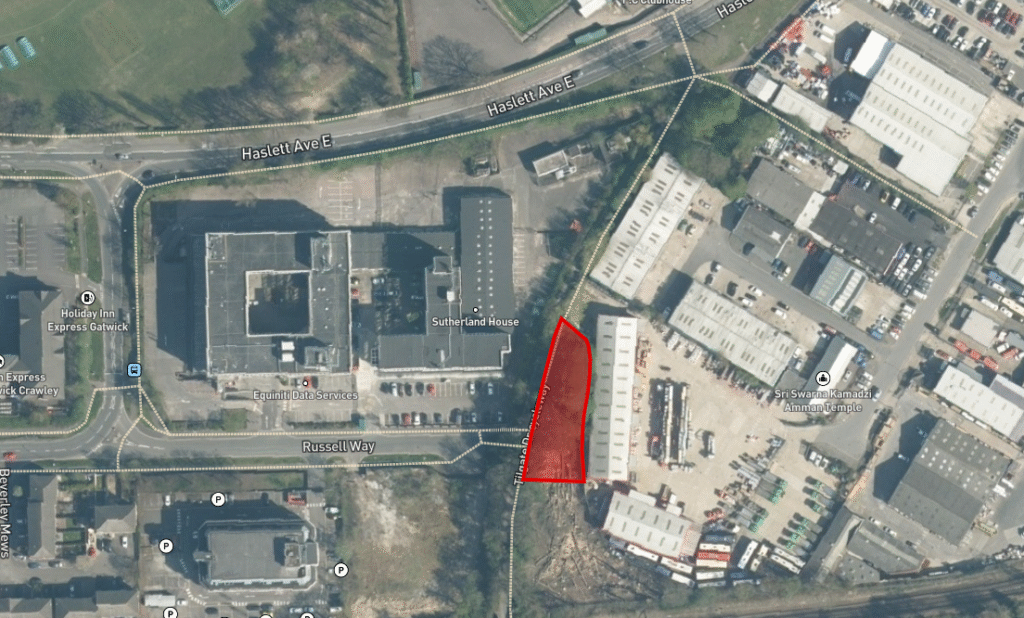 Property for sale Aerial view of an industrial area in Crawley bordered by roads, buildings, and green space. A triangular plot of land for sale Crawley is highlighted in red near Russell Way, surrounded by warehouses and office buildings. Presented by Palace Auctions