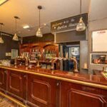 Property for sale A traditional pub bar with wooden counters and beer taps, glassware neatly arranged, pendant lights overhead, and a sign reading “Welcome to The Burton House”—a classic public house conversion in the Newcastle area. Presented by Palace Auctions