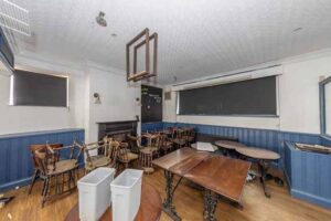 Property for sale A cluttered room with wooden tables and chairs, two white bins, blue paneling, covered windows, and an unlit fireplace hints at a traditional public house conversion in the Newcastle area. The space appears unused or in transition. Presented by Palace Auctions