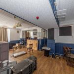 Property for sale A cluttered, empty room with blue wainscoting, scattered chairs, wooden flooring, and bright daylight—ideal for a traditional public house conversion in the Newcastle area. Presented by Palace Auctions