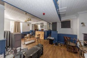 Property for sale A cluttered, empty room with blue wainscoting, scattered chairs, wooden flooring, and bright daylight—ideal for a traditional public house conversion in the Newcastle area. Presented by Palace Auctions