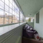 Property for sale A narrow, enclosed porch with paned windows and light green wooden walls hints at a traditional public house conversion; beyond the cluttered corner, a brick house and greenery suggest the charm of the Newcastle area. Presented by Palace Auctions