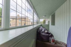 Property for sale A narrow, enclosed porch with paned windows and light green wooden walls hints at a traditional public house conversion; beyond the cluttered corner, a brick house and greenery suggest the charm of the Newcastle area. Presented by Palace Auctions