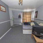 Property for sale A small bedroom with gray walls, patterned bedding, a TV on a wooden table, drying rack, wall art, and a window with brown patterned curtains letting in daylight—ideal for a traditional public house conversion in the Newcastle area. Presented by Palace Auctions