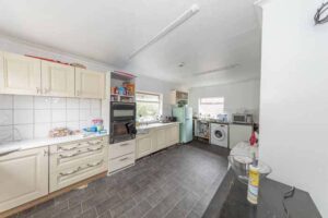 Property for sale A bright kitchen in a traditional public house conversion, featuring cream cabinets, a black oven, washing machine, and fridge. Countertops hold various items and groceries; a window lets in natural light over dark tiled floors. Located in the Newcastle area. Presented by Palace Auctions