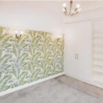 Property for sale A bright room in this Altrincham period flat features leafy green palm-patterned wallpaper, built-in white wardrobes with shelves, light gray carpet, and modern wall and ceiling lights. Presented by Palace Auctions