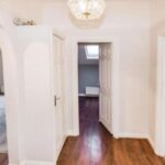 Property for sale A bright hallway in this Altrincham period flat boasts white walls, wood flooring, and a chandelier. Two doors reveal adjoining rooms—one with a skylight and radiator, another with a partially visible carpeted space. Presented by Palace Auctions