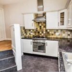 Property for sale Modern kitchen in a Bowdon 4-bed flat, featuring white cabinets, a built-in oven, gas stove, and stainless steel range hood. Multi-colored tile backsplash and dark countertops add style to this attractive WA14 residential investment property. Presented by Palace Auctions