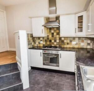 Property for sale Modern kitchen in a Bowdon 4-bed flat, featuring white cabinets, a built-in oven, gas stove, and stainless steel range hood. Multi-colored tile backsplash and dark countertops add style to this attractive WA14 residential investment property. Presented by Palace Auctions