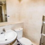 Property for sale A modern bathroom in this Altrincham period flat features a white sink, toilet, wall-mounted mirror, beige tiled walls, and a metallic heated towel rail on the right. Presented by Palace Auctions