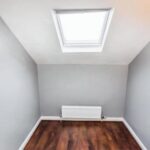 Property for sale A small, empty room with gray walls, a wooden floor, radiator on the back wall, and a skylight window in the sloped ceiling letting in natural light—ideal for a Bowdon investment property or as part of a Heald Road apartment auction. Presented by Palace Auctions