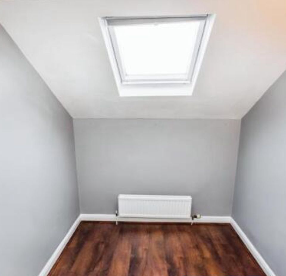 Property for sale A small, empty room with gray walls, a wooden floor, radiator on the back wall, and a skylight window in the sloped ceiling letting in natural light—ideal for a Bowdon investment property or as part of a Heald Road apartment auction. Presented by Palace Auctions