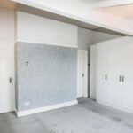 Property for sale A bright, empty room with light gray carpet, white walls, a blue patterned accent wall, two white doors, and a large white wardrobe with black handles—ideal for those seeking a WA14 residential investment on Heald Road or Bowdon investment property. Presented by Palace Auctions