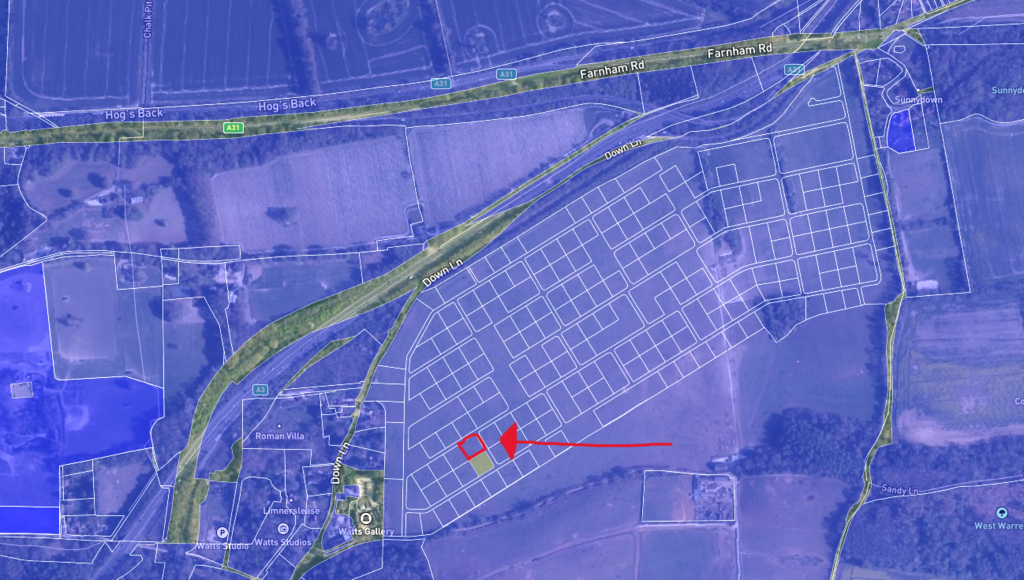 Property for sale A satellite map with outlined plots; a bold red arrow points to a specific rectangular plot near the center, highlighted with a red circle. Main roads border this land auction site in Guildford, surrounded by fields and buildings. Presented by Palace Auctions