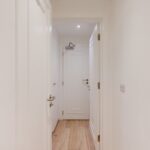 Property for sale A narrow hallway with white walls and doors, light wood flooring, and a glimpse of a ceiling light at the far end near a closed door—ideal for a high yield London property or Edgware Road property investment. Presented by Palace Auctions