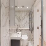 Property for sale Modern bathroom with marble walls, a white sink and cabinet, wall-mounted mirror, chrome towel radiator, and bright lighting—ideal for a mixed-use freehold London property near Edgware Road; wooden floor visible through the doorway. Presented by Palace Auctions