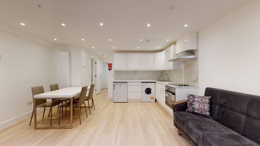 Property for sale Modern open-plan kitchen and living area with white cabinets, built-in appliances, a dining table for six, and a dark sofa on light wooden floors—ideal for an Edgware Road property investment or multi-unit rental property. Presented by Palace Auctions